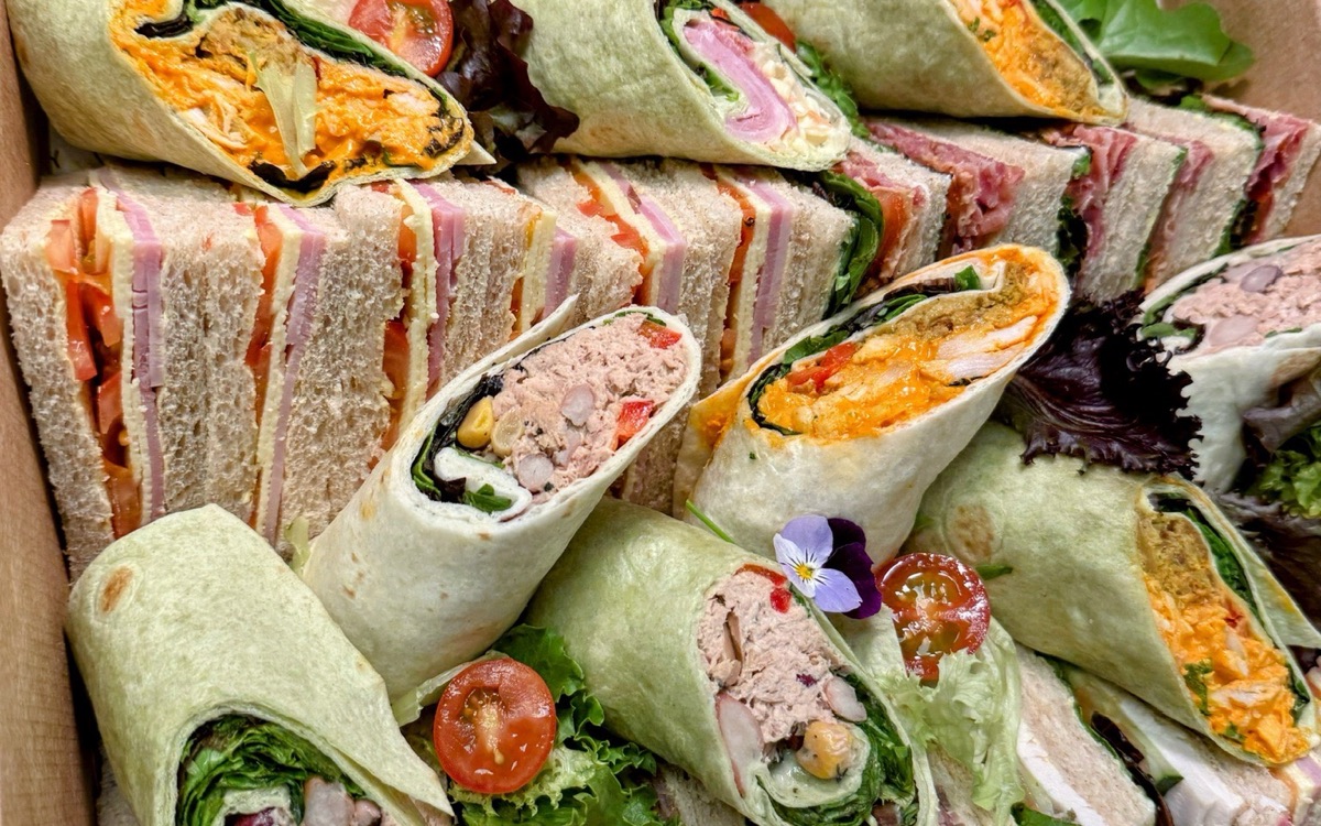 A catering box of club sandwiches and filled wraps &mdash; chicken tikka, tuna and ham &mdash; garnished with salad, cherry tomatoes and edible flowers