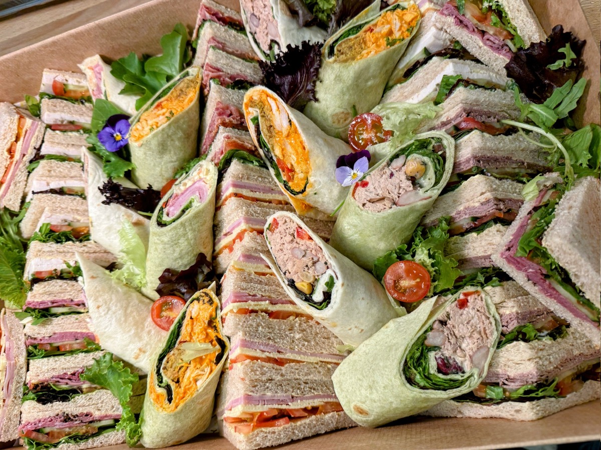 A catering box of sandwiches and wraps, arranged and garnished