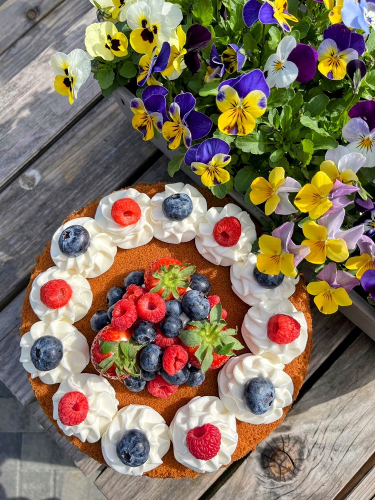 Sponge cake topped with a wreath of meringues, cream and fresh berries