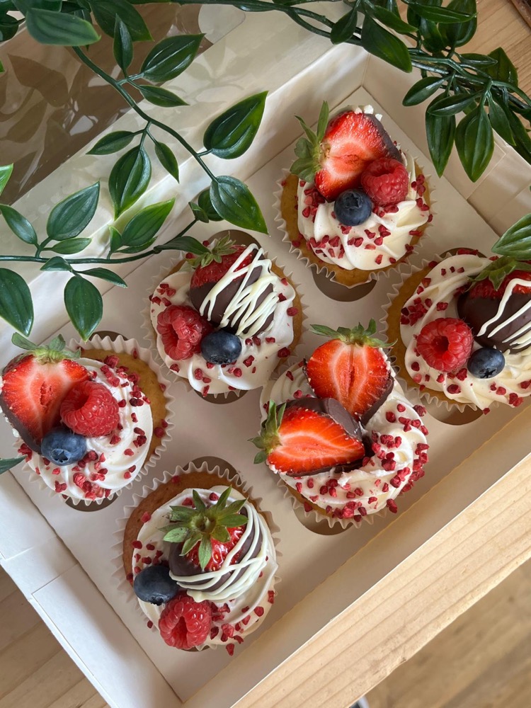 Cupcakes topped with cream, strawberries, raspberries and blueberries