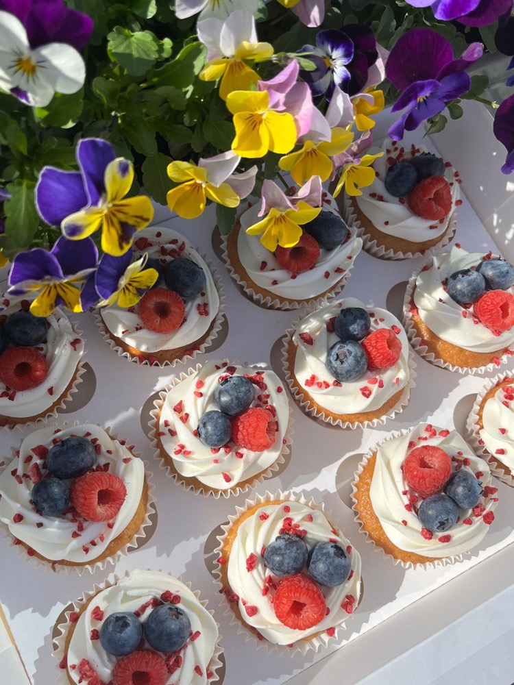 Cupcakes topped with cream, raspberries and blueberries, surrounded by pansies