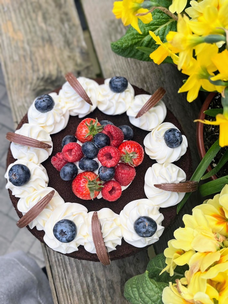 Chocolate cake decorated with cream swirls, chocolate curls, blueberries and fresh berries