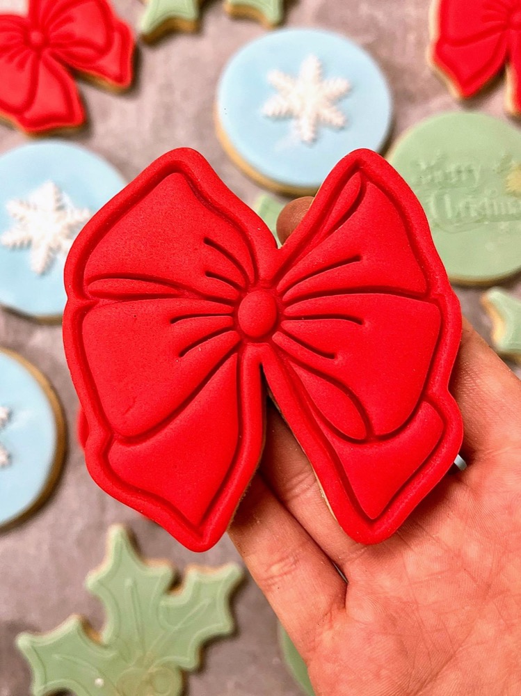 Hand holding an iced bow-shaped Christmas cookie among snowflake and holly biscuits