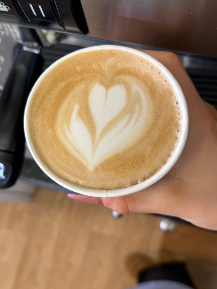 A flat white with a heart poured into the foam, held by the coffee machine